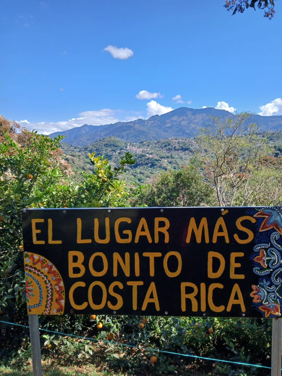 Rótulo pintado a mano que dice El lugar más bonito de Costa Rica, con las montañas de Acosta de fondo