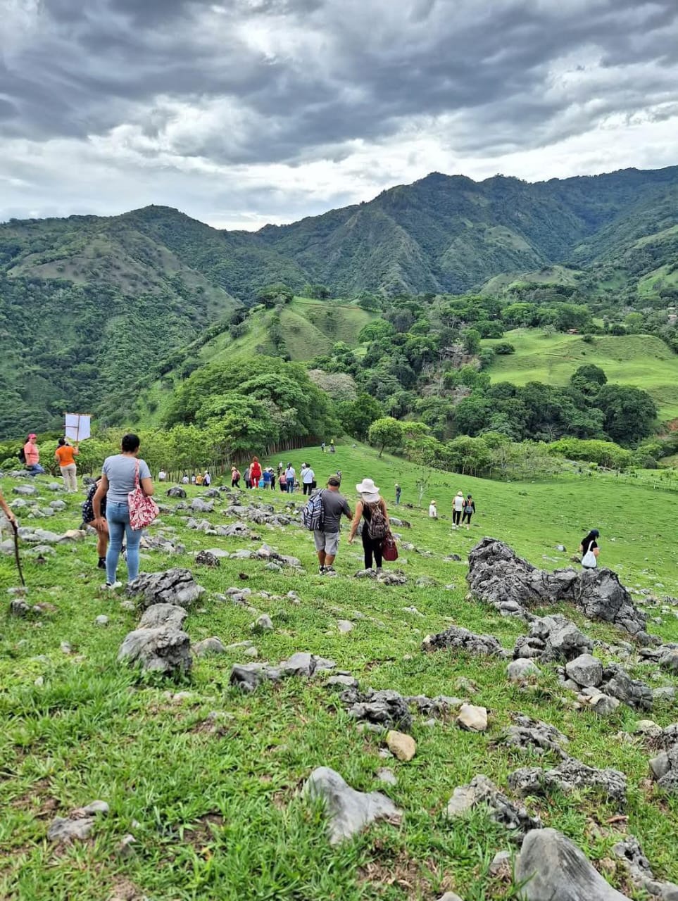 Vecinos y vecinas caminando por un sendero rural entre montañas verdes de Acosta